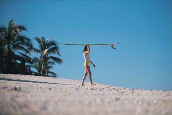 woman-carrying-surfboard-on-head-towards-ocean-at-namotu-island-fiji